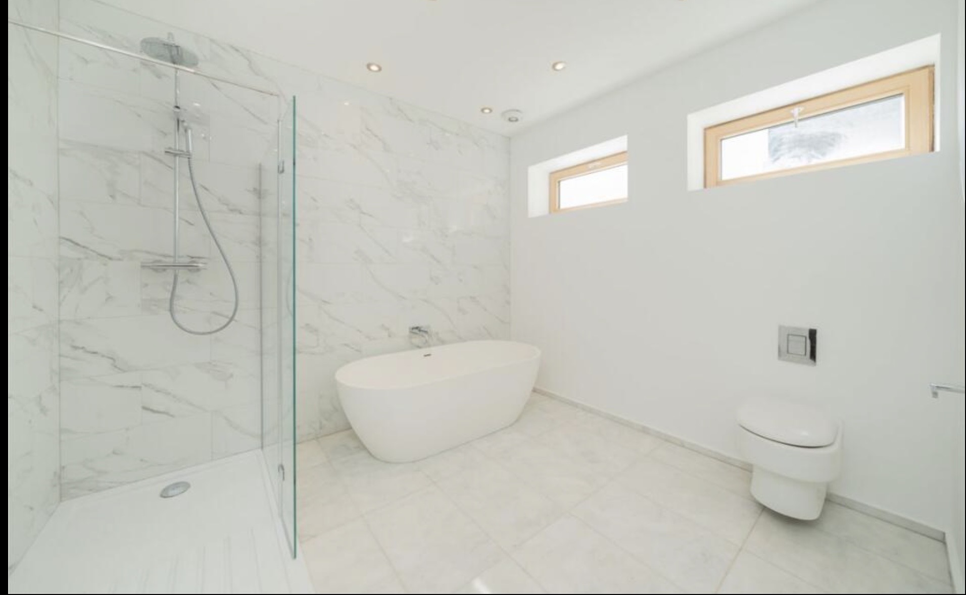 Refurbished bathroom with marble tiles, freestanding bath and walk-in glass shower